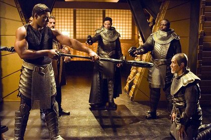 Christopher Judge holds a weapon to a man's head in Stargate SG-1