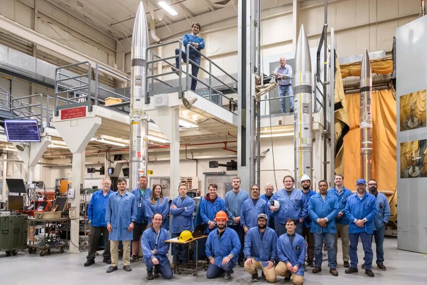 The NASA support team poses in blue shirts next to three APEP sounding rockets.